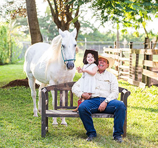 A grandfather and his niece sitting on a bench with a white horse behind them
